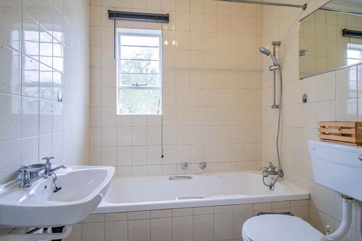 A dated bathroom featuring a standard bathtub, pedestal basin, and toilet with full-height wall tiling, offering potential for a modern renovation.