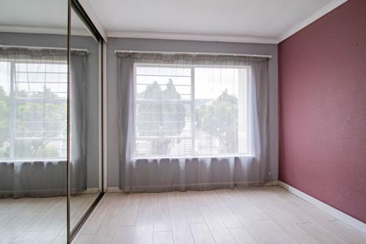 An empty bedroom featuring light laminate flooring, a large mirrored sliding wardrobe, and a window fitted with security bars.