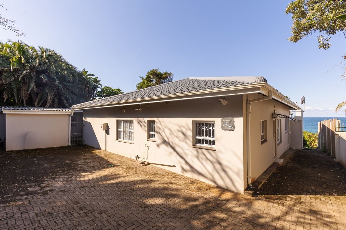 Rear exterior view of the property featuring a paved courtyard, tiled roof, and security-fitted windows with a partial ocean view.