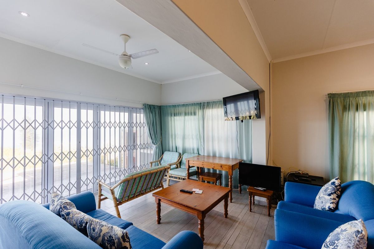 A spacious living area featuring tiled flooring, a ceiling fan, and large sliding doors secured with a metal security gate.