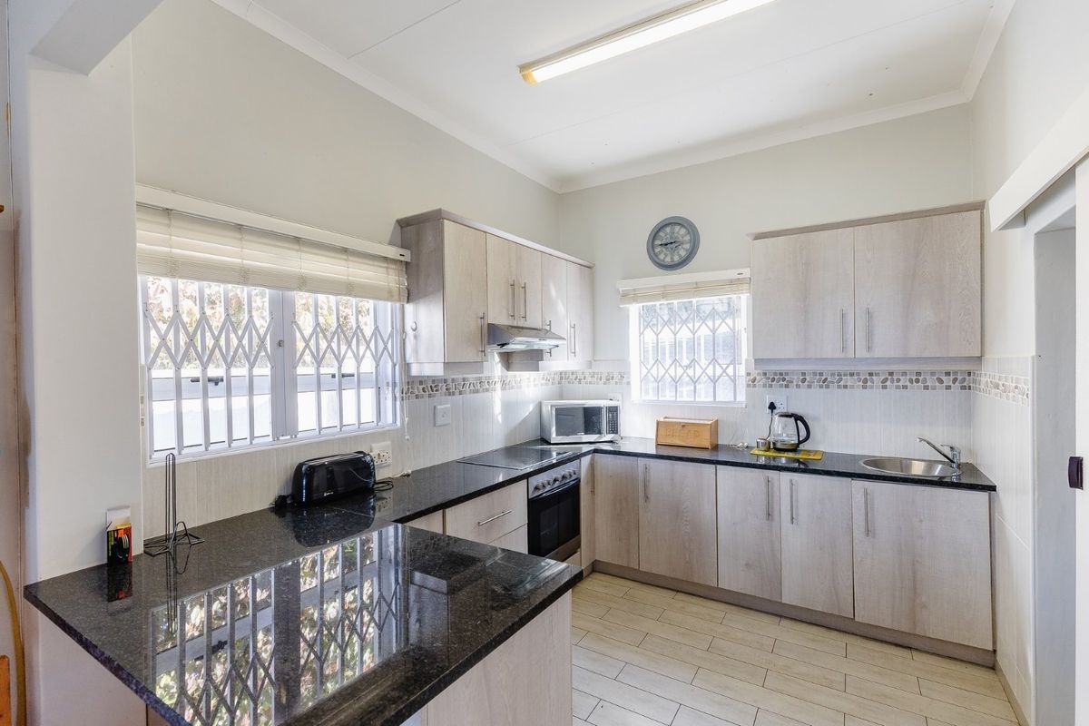 A functional kitchen featuring light wood-finish cabinetry, dark granite countertops, built-in oven, extractor fan, and tiled flooring with security-fitted windows.