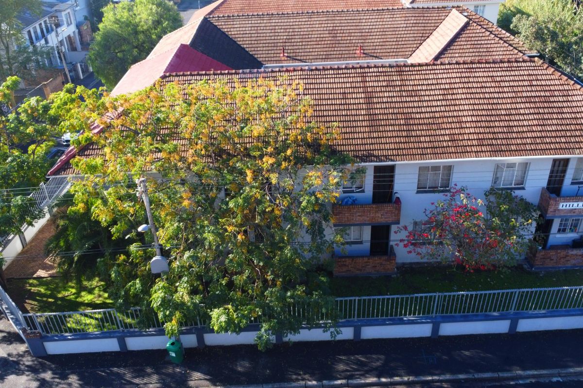 Aerial view of a multi-story apartment building featuring a tiled roof, brick balconies, and secure perimeter fencing with a boundary wall.