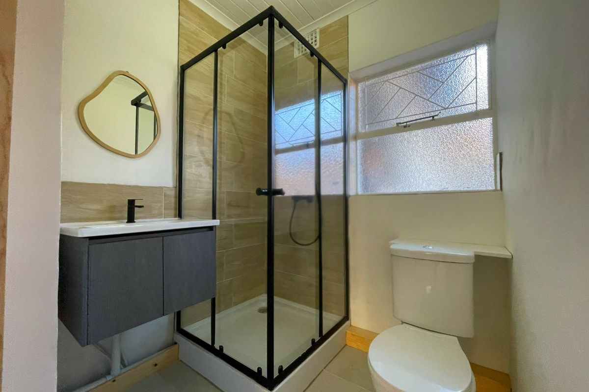 Modernized bathroom featuring a black-framed shower enclosure, wall-mounted vanity, and toilet, with neutral tiling and obscured glass window for privacy.