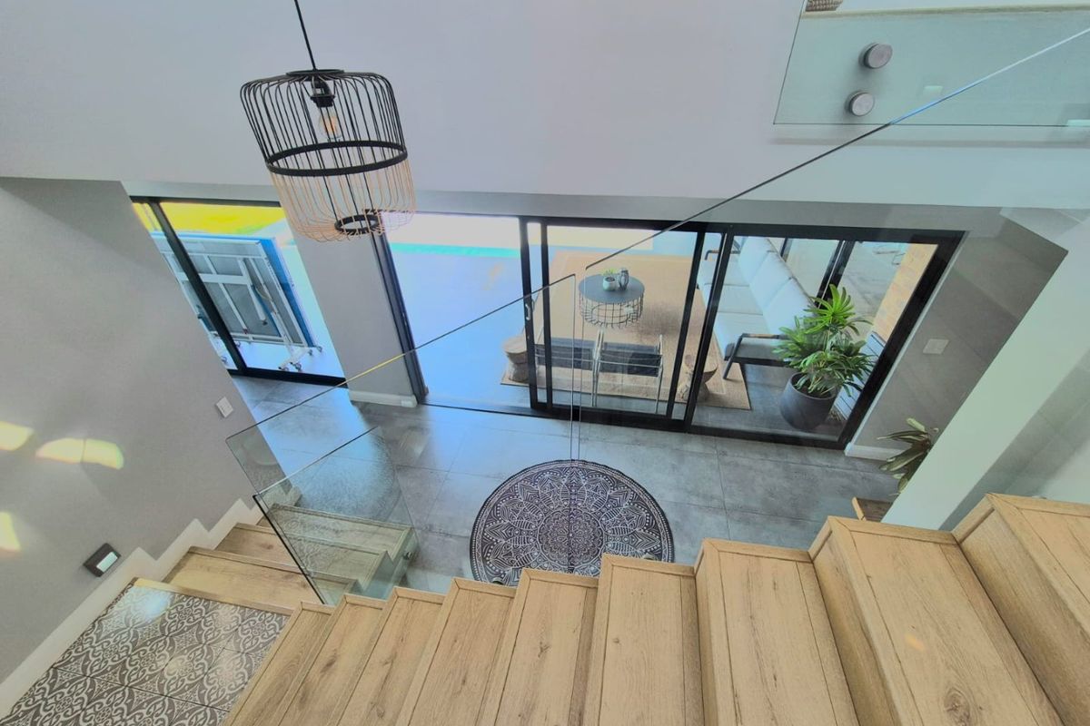 Modern open-plan living area featuring a timber staircase with glass balustrade, large sliding doors leading to the patio, and contemporary tiled flooring.
