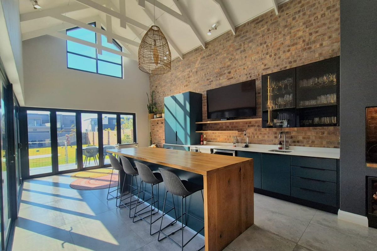 Modern kitchen featuring exposed brick walls, vaulted ceilings with exposed rafters, sleek cabinetry, stone countertops, and large bi-fold doors opening to the garden.