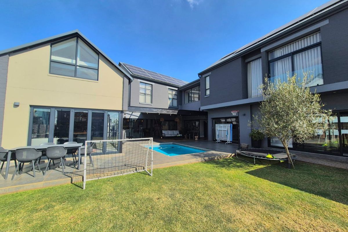 Spacious rear exterior featuring a well-maintained lawn, a swimming pool, paved patio area, and modern multi-story building architecture with solar panels.