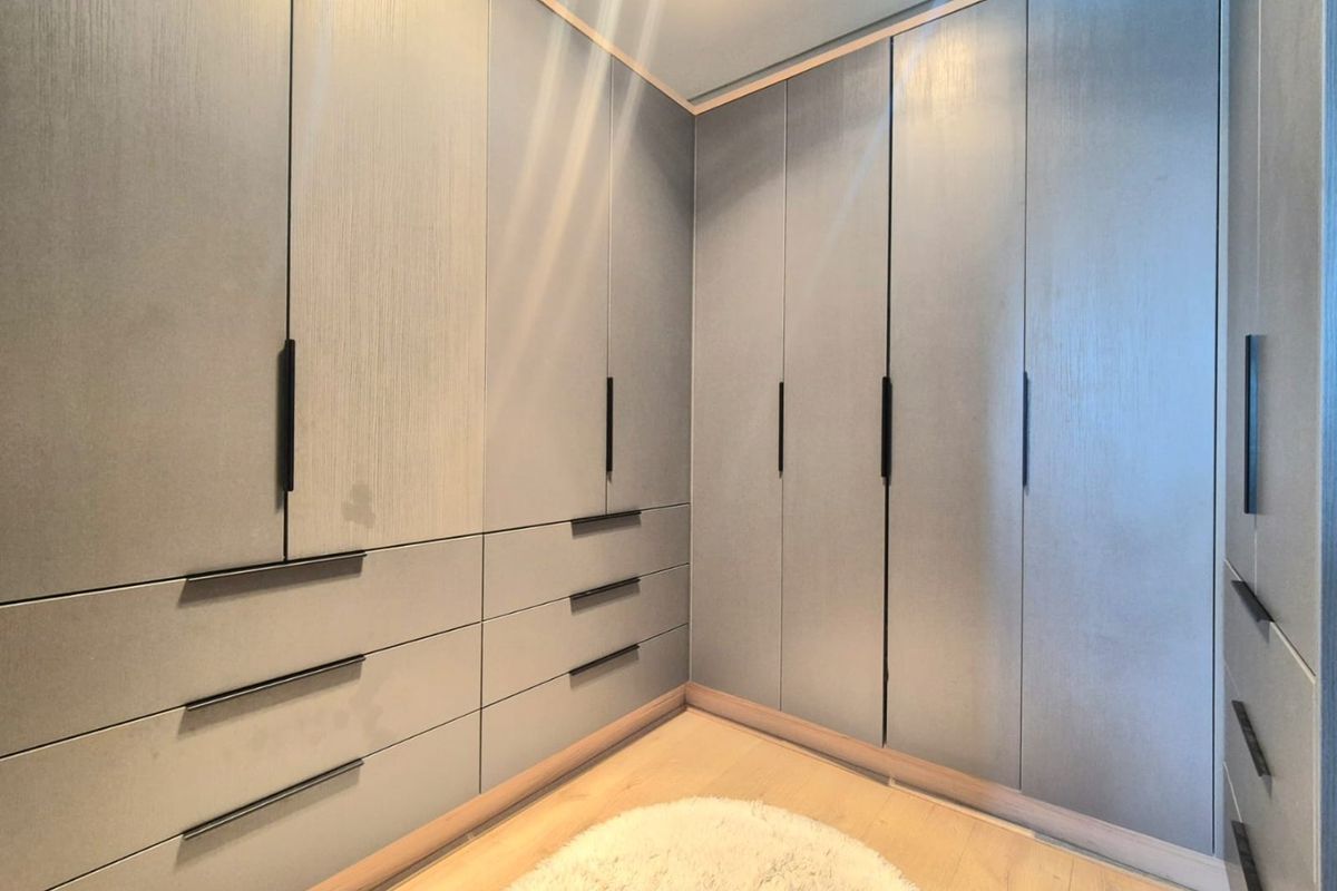 A modern walk-in closet or bedroom area featuring extensive floor-to-ceiling built-in cabinetry with sleek matte grey finishes and integrated drawer storage.