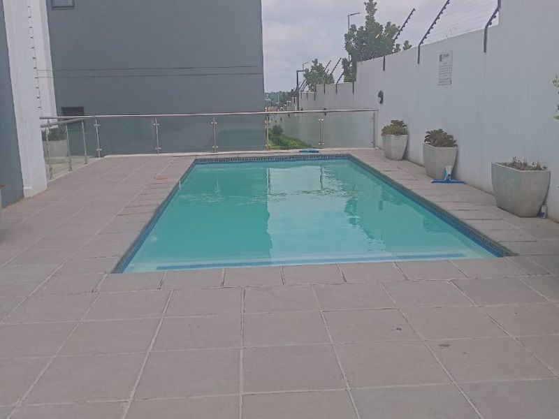 A clean, modern swimming pool area featuring a paved deck, glass balustrade, and secure perimeter walling.