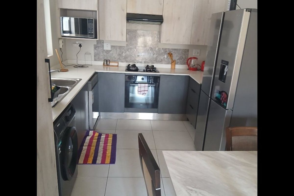 Modern kitchen featuring light wood and grey cabinetry, stone countertops, built-in oven, gas hob, extractor fan, and integrated microwave with tiled flooring.