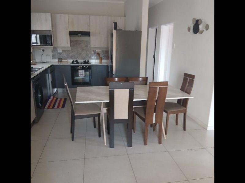 Open-plan kitchen and dining area featuring modern cabinetry, built-in oven, hob, extractor fan, and neutral tiled flooring throughout.