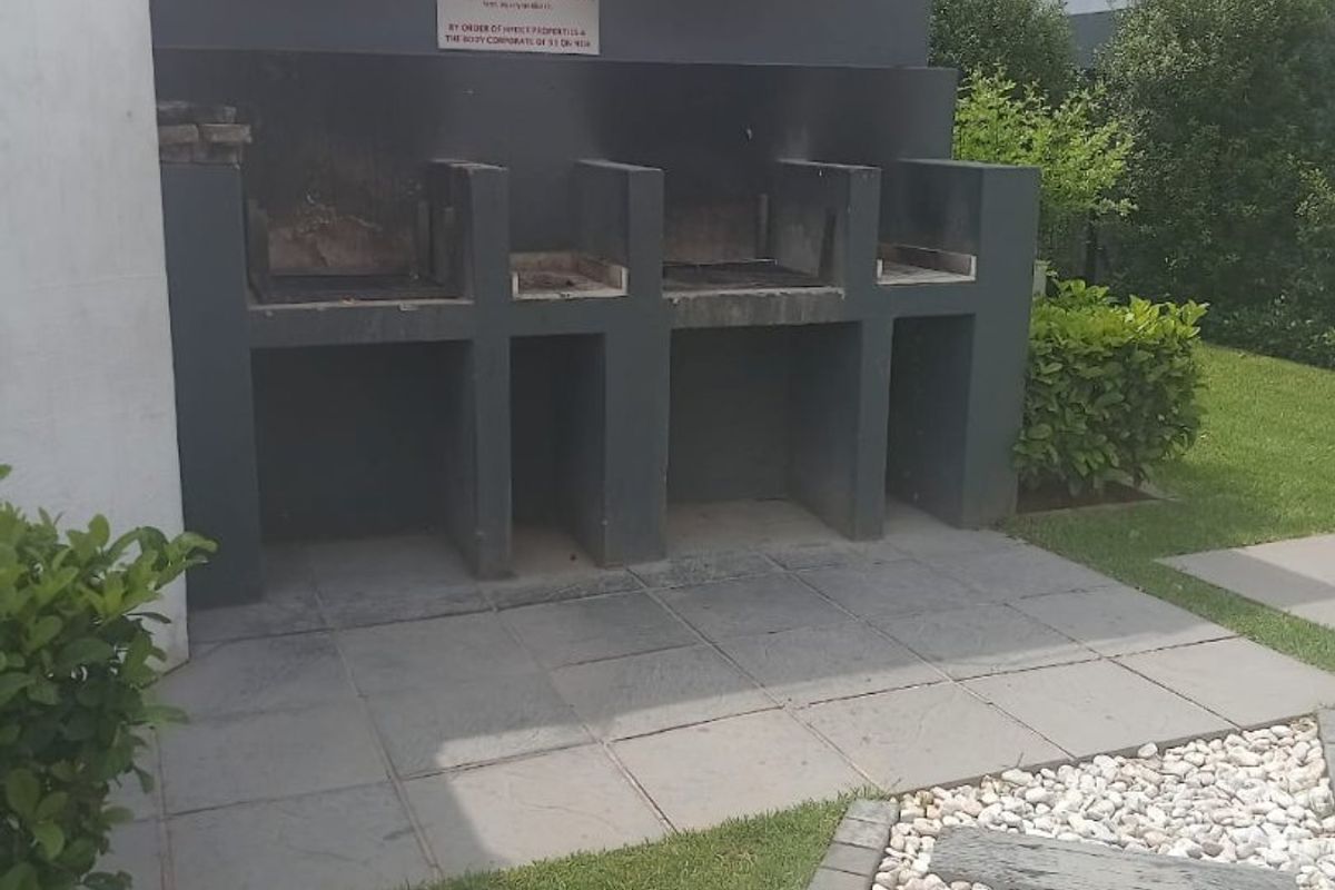 Outdoor communal area featuring a built-in braai station, paved patio, and landscaped garden with a stone pathway.