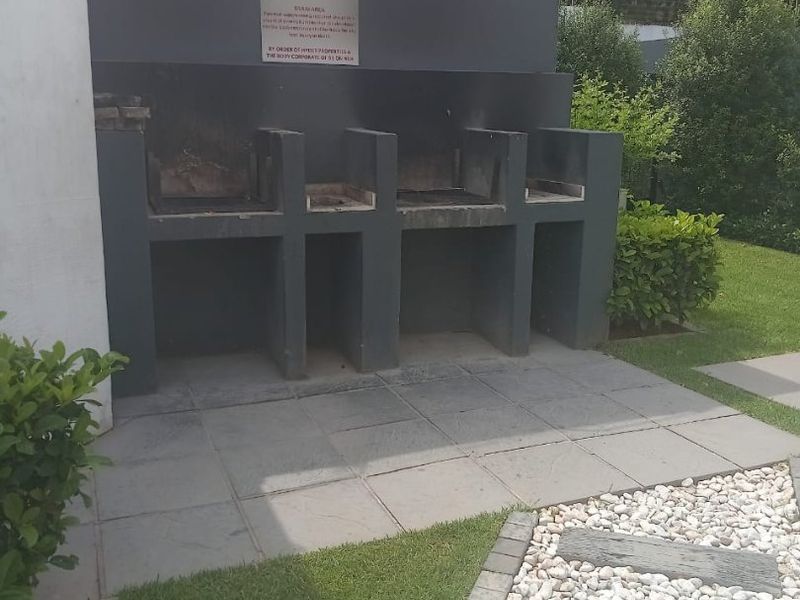 Outdoor communal area featuring a built-in braai station, paved patio, and landscaped garden with a stone pathway.