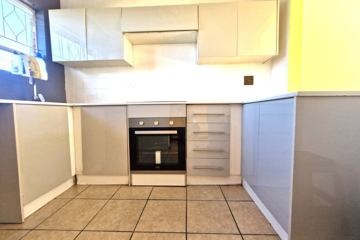 A functional kitchen featuring modern grey cabinetry, built-in oven, tiled backsplash, and ceramic floor tiles, offering a clean and practical workspace.