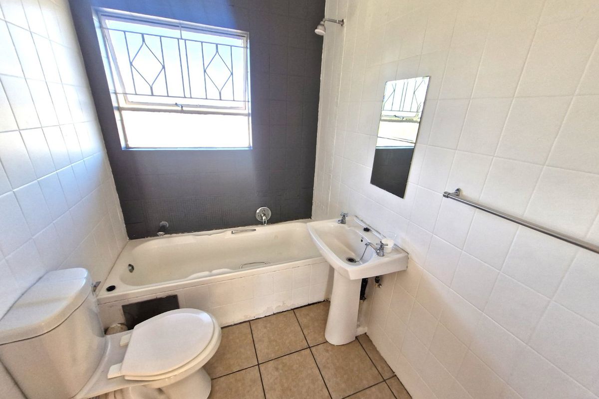 A functional bathroom featuring a bathtub, pedestal basin, and toilet with tiled finishes, requiring some maintenance and cosmetic updates.
