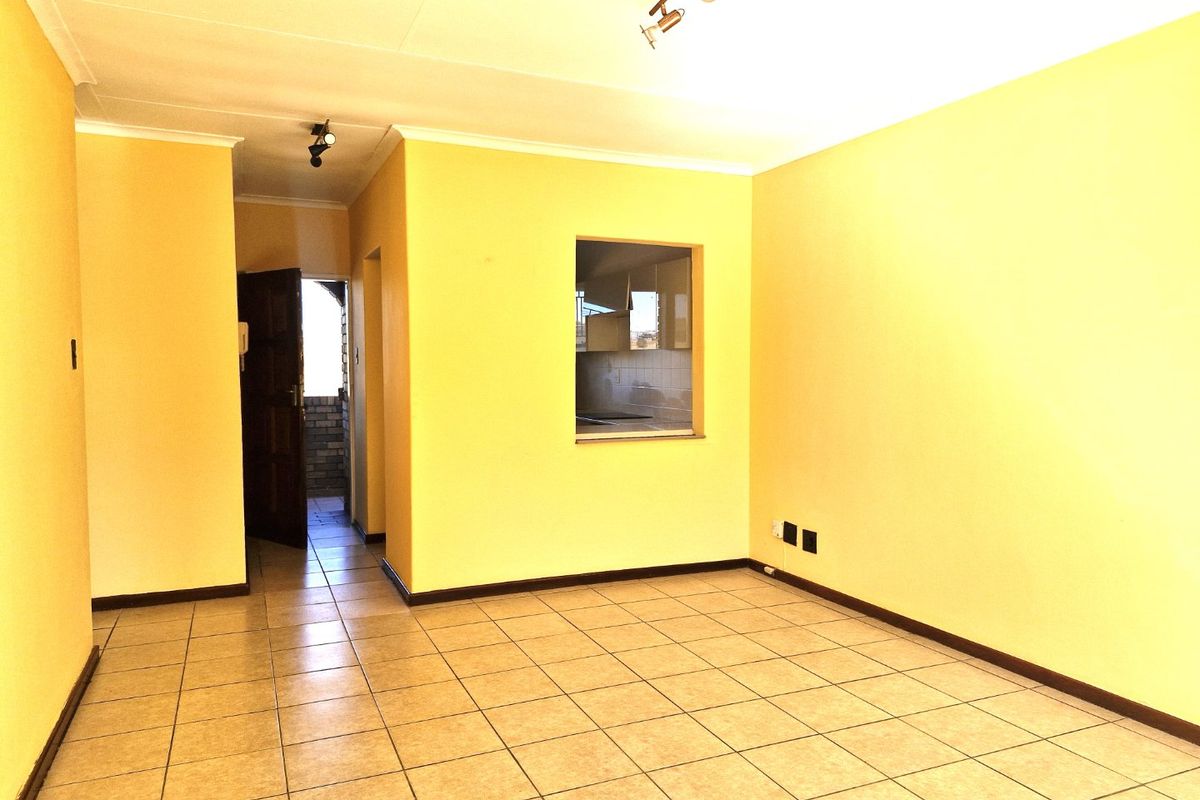 An empty living room featuring ceramic floor tiles, coving, and a convenient pass-through window connecting to the kitchen area.