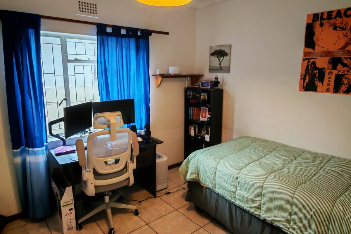 A functional bedroom featuring tiled flooring and a window fitted with security bars, providing a practical space for rest or study.