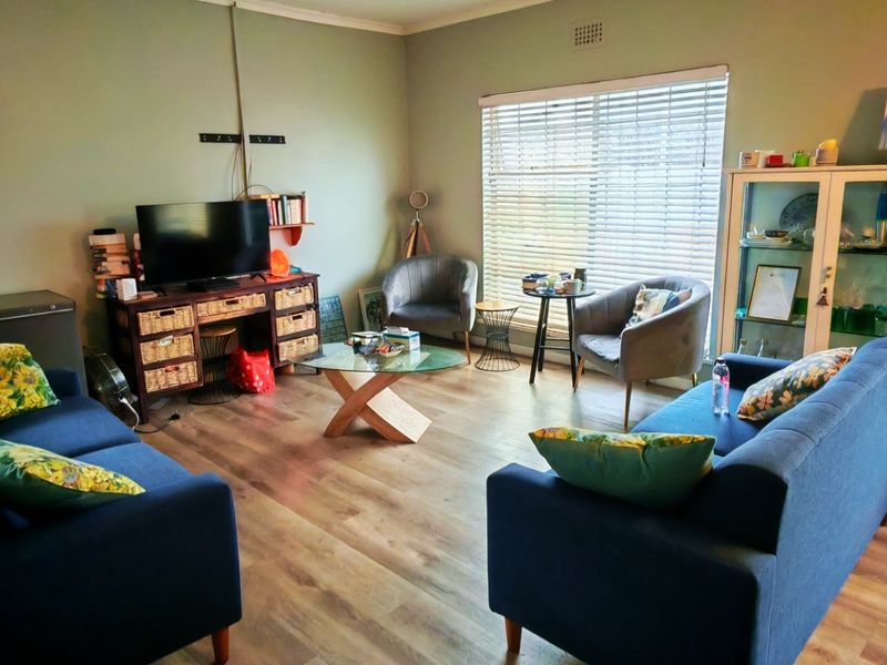 A comfortable living room featuring light-toned laminate flooring and large windows fitted with venetian blinds, providing a bright and functional space.