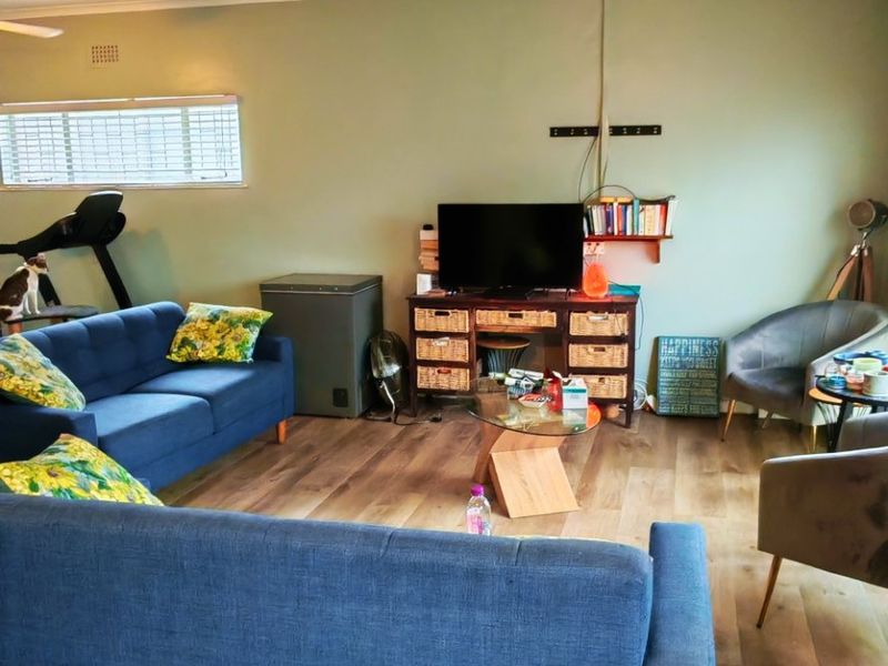 A spacious living room featuring wood-look laminate flooring, a ceiling fan, and large windows with blinds, offering a comfortable and functional living space.