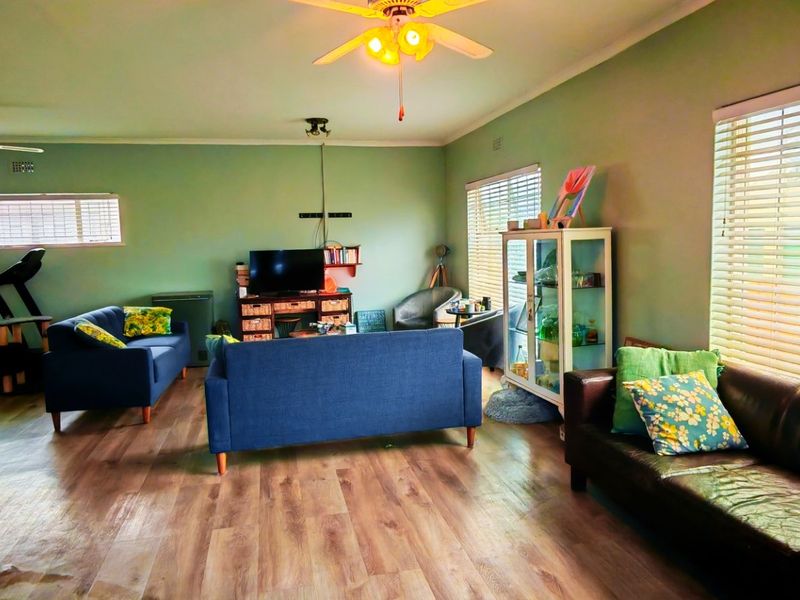 Spacious living room featuring laminate flooring, ceiling fans, and large windows with venetian blinds, offering a comfortable and functional layout.