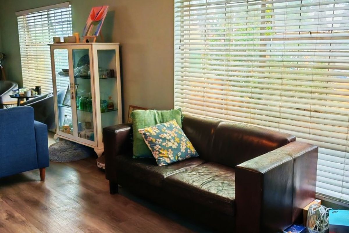 A living room featuring laminate flooring, ceiling fan, and large windows with fitted venetian blinds.