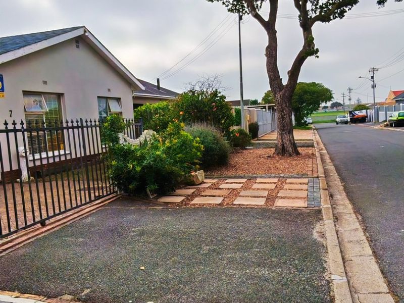 Street view of the property frontage featuring a paved driveway, metal perimeter fencing, and a mature tree along the sidewalk.