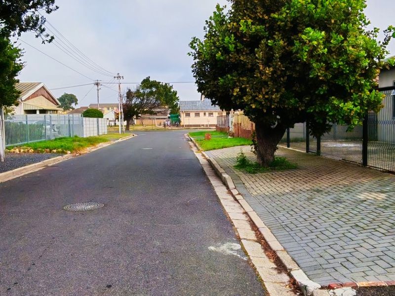 A view of the residential street showing the paved road, curb, and perimeter fencing of the property.