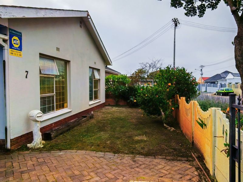 Front exterior view of the property featuring a paved driveway, small garden area, and secure boundary wall with metal gate access.