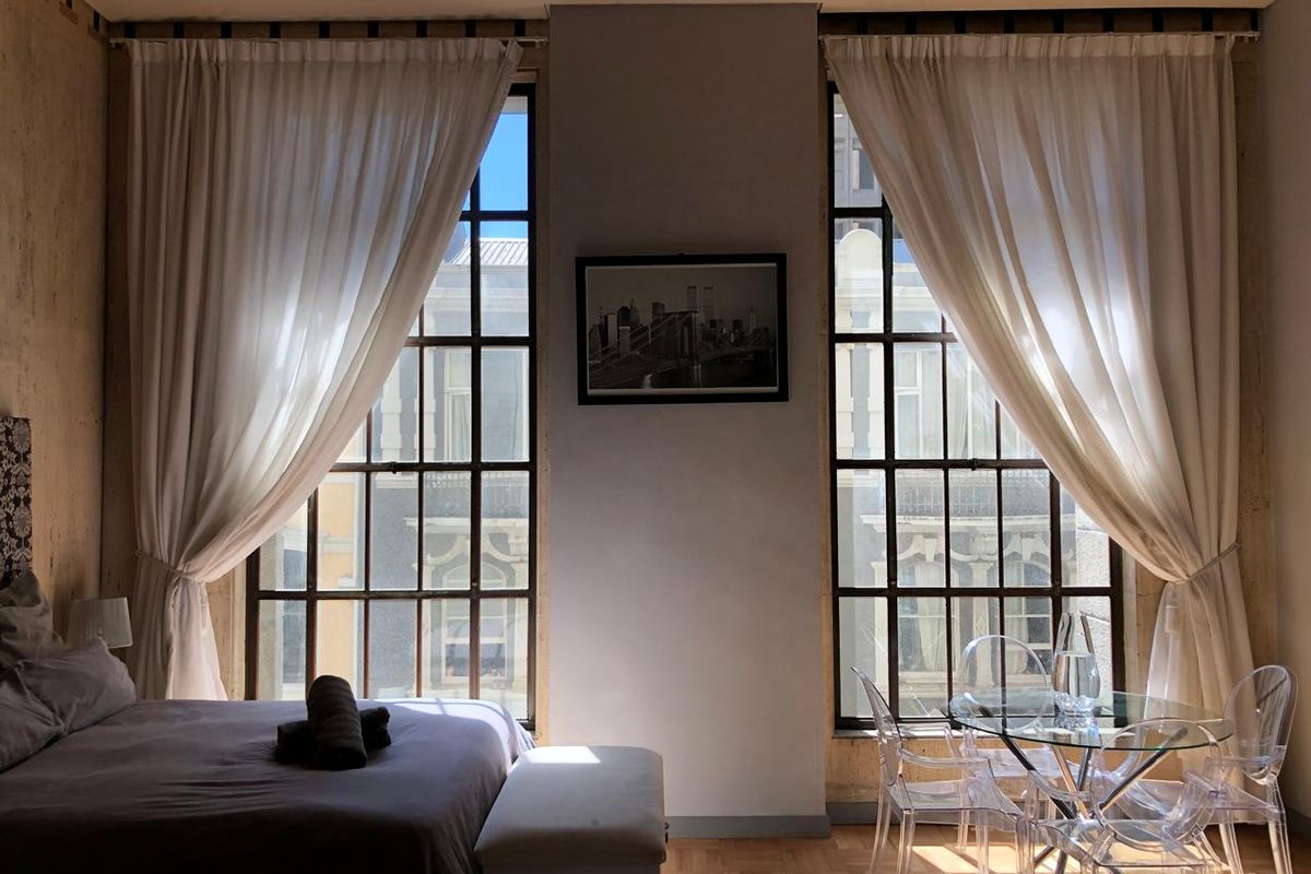 A well-lit bedroom featuring classic parquet flooring and large, multi-pane windows that provide ample natural light and urban views.