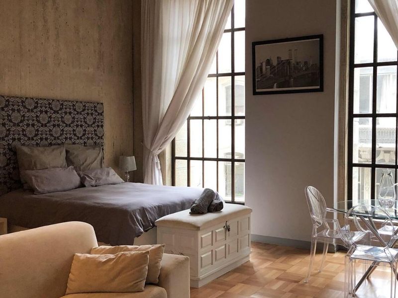 A bright open-plan studio apartment featuring beautiful parquet flooring, high ceilings, and large industrial-style windows that provide ample natural light.