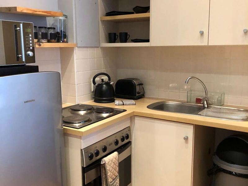 Compact kitchen featuring built-in oven, electric hob, stainless steel sink, and a mix of upper cabinetry and open shelving with tiled backsplash.
