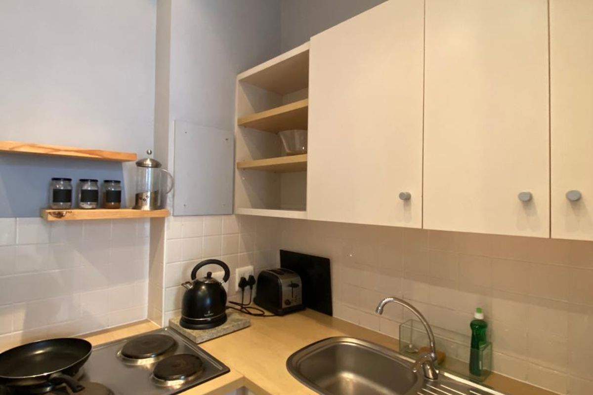 Compact kitchen featuring white cabinetry, wooden countertops, a stainless steel sink, and a built-in electric hob and oven with a tiled backsplash.