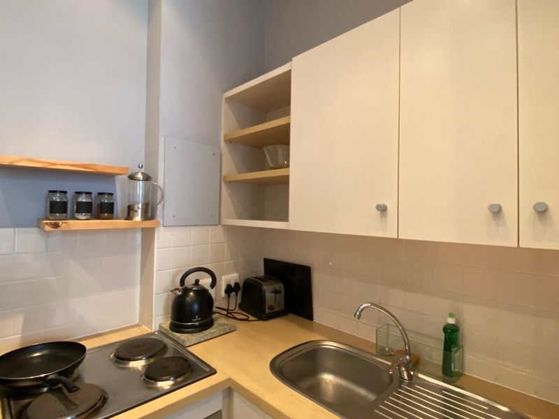 Compact kitchen featuring white cabinetry, wooden countertops, a stainless steel sink, and a built-in electric hob and oven with a tiled backsplash.