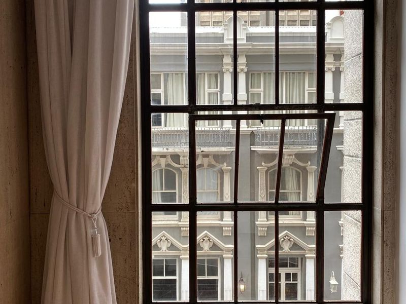 A view through a large industrial-style steel window frame, showcasing urban architecture with natural light and high-quality finishes.