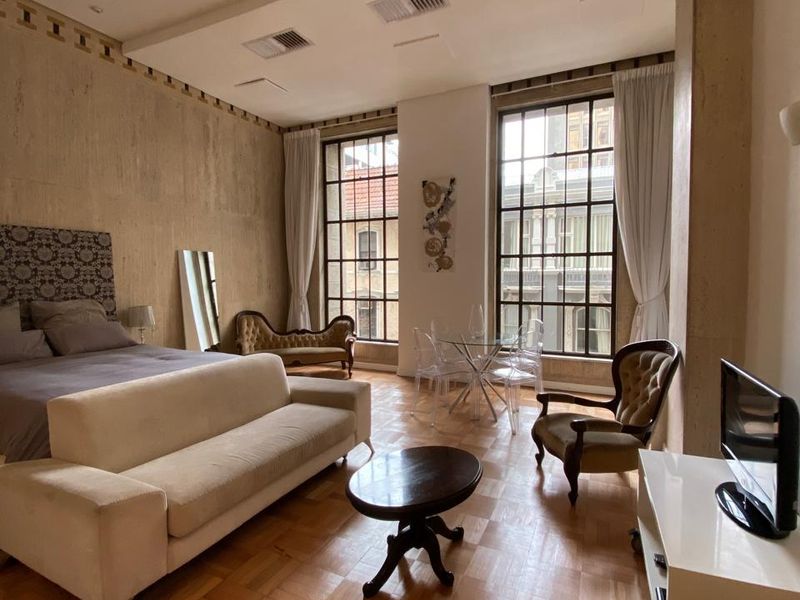 Spacious bedroom featuring high ceilings, parquet flooring, and large industrial-style windows that provide ample natural light and an urban outlook.