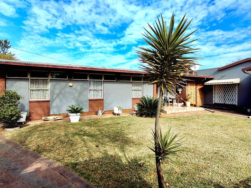 Rear view of the property featuring a paved driveway, lawn area, and brick and painted exterior walls with security features.