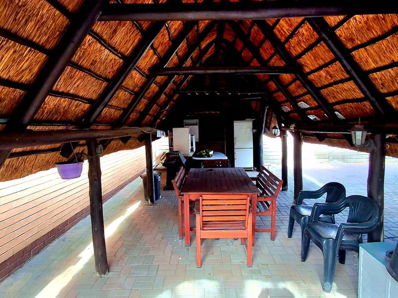 Covered outdoor patio area featuring a traditional thatch roof, timber support beams, and paved flooring, ideal for outdoor dining and entertainment.
