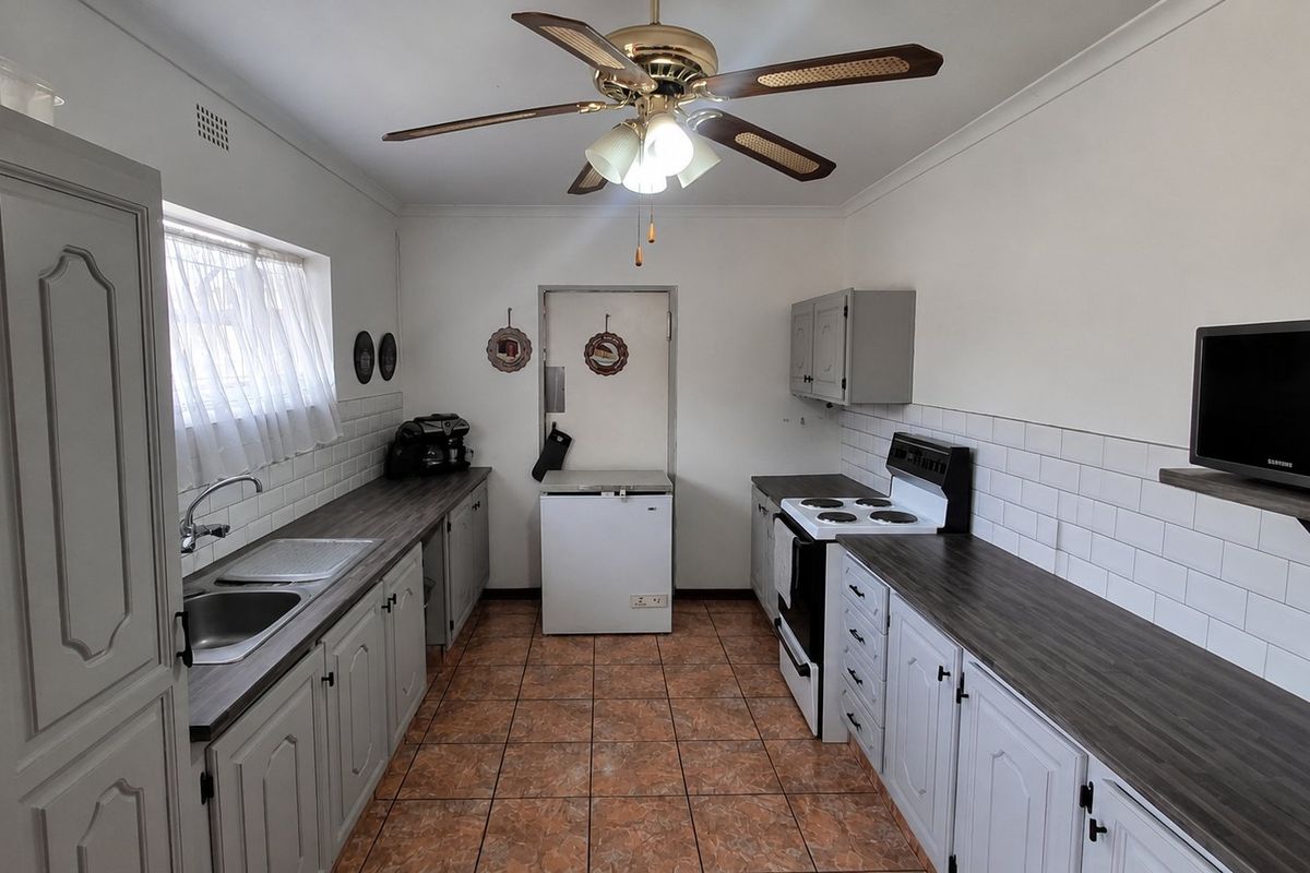 A functional kitchen featuring subway tile backsplashes, laminate countertops, built-in cabinetry, and a ceiling fan, providing a practical workspace with classic finishes.