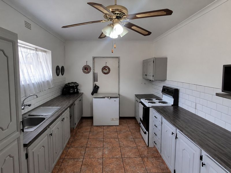 A functional kitchen featuring subway tile backsplashes, laminate countertops, built-in cabinetry, and a ceiling fan, providing a practical workspace with classic finishes.
