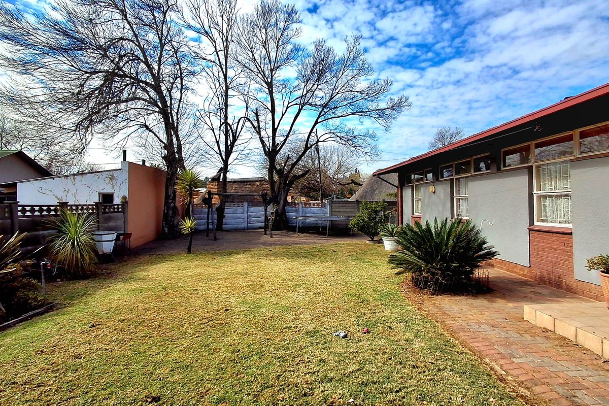 A rear garden view featuring a brick-paved patio area, established trees, and a precast concrete boundary wall.