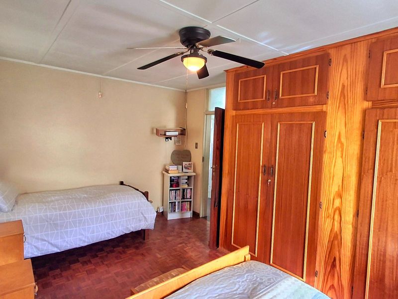 A bedroom featuring classic parquet flooring, a ceiling fan, and extensive built-in wooden cabinetry providing ample storage space.
