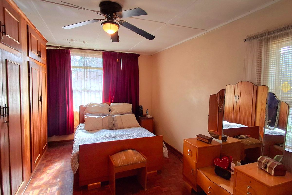 A bedroom featuring parquet flooring, built-in wooden cupboards, and a ceiling fan, with visible water staining on the ceiling.