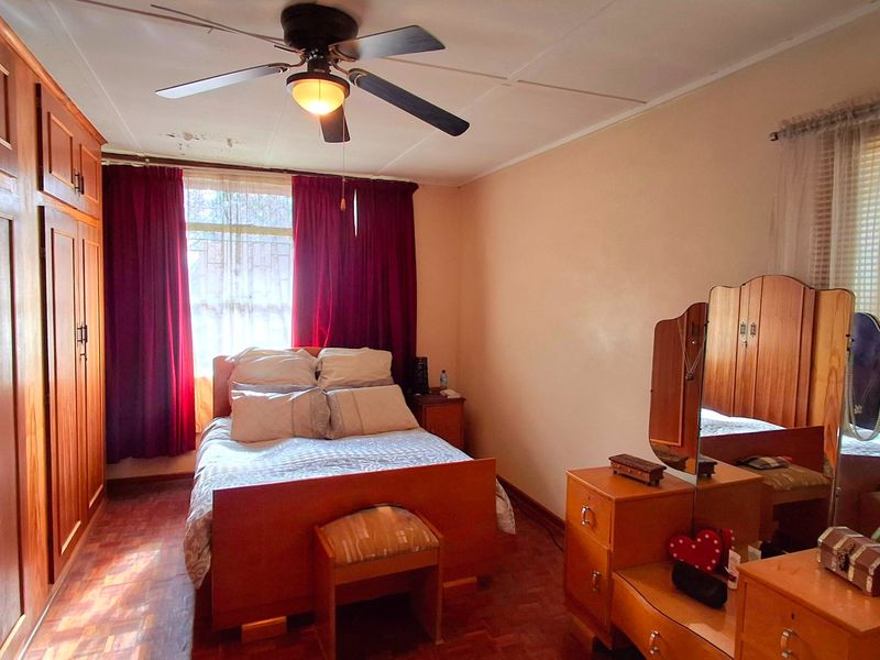 A bedroom featuring parquet flooring, built-in wooden cupboards, and a ceiling fan, with visible water staining on the ceiling.