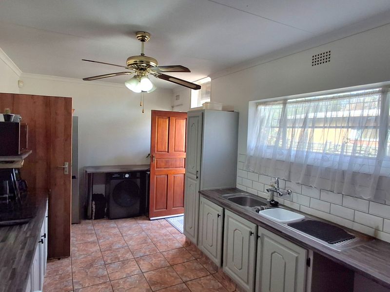 A functional kitchen featuring tiled flooring, subway tile backsplash, laminate countertops, and built-in cabinetry with a ceiling fan.