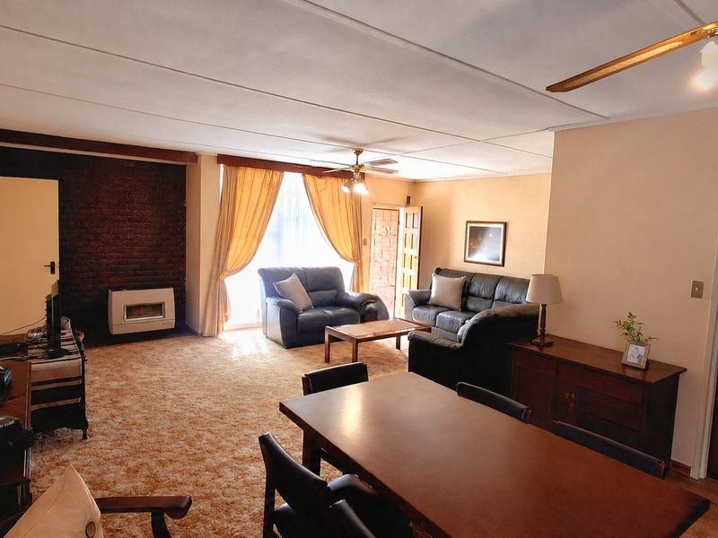 Spacious open-plan living and dining area featuring a brick fireplace, gas heater, and ceiling fan, offering a functional layout with potential for modernization.