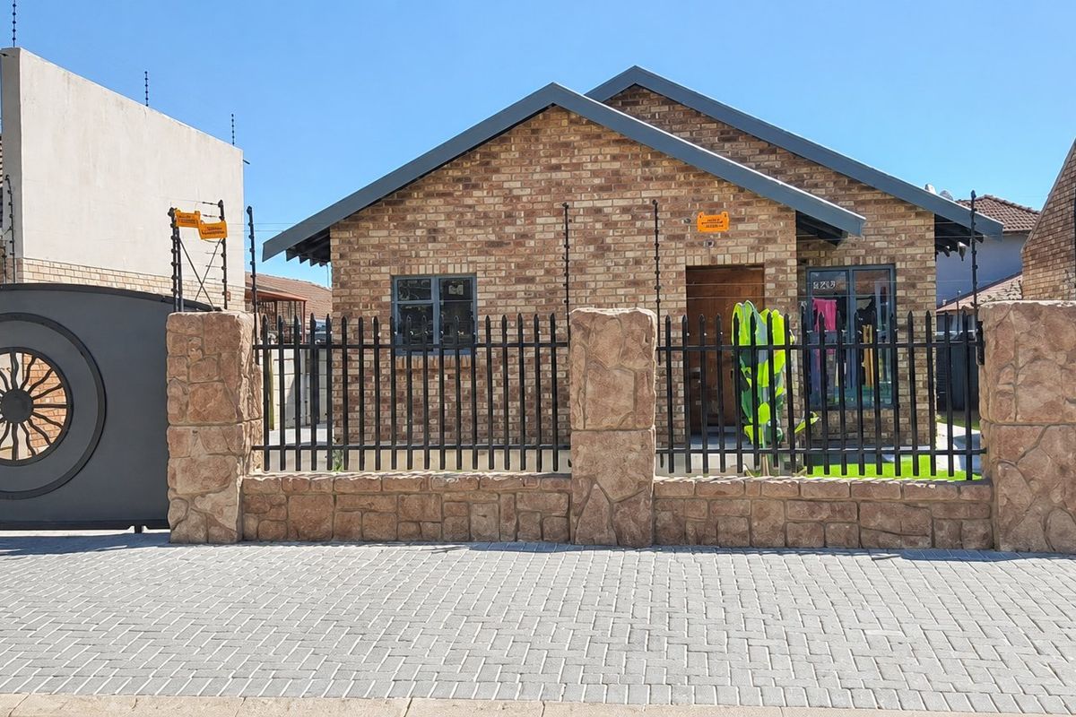 Front view of a face brick house featuring a secure boundary wall, electric fencing, and a paved driveway entrance.