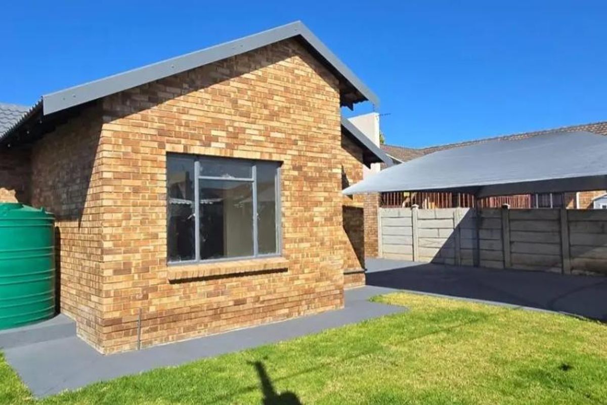 Rear exterior view featuring a face brick house, a water storage tank, a paved area with a shade cloth carport, and a lawn.
