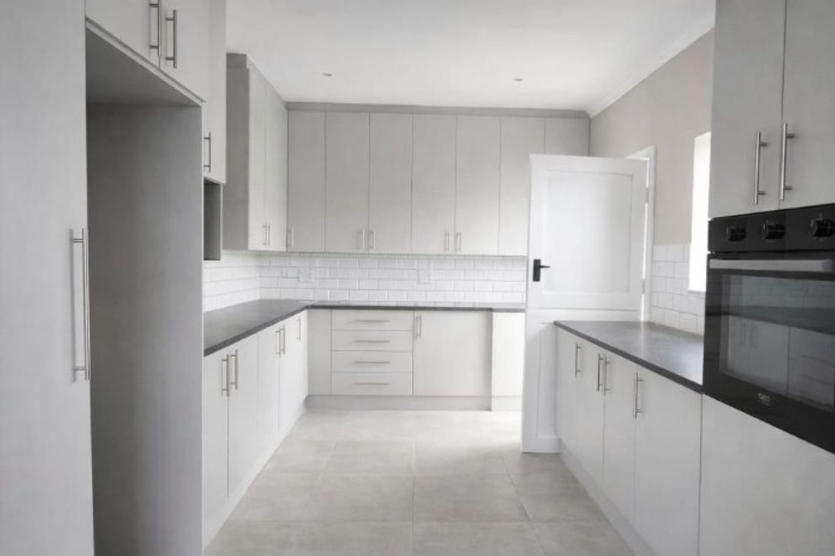 Modern kitchen featuring light grey cabinetry, subway tile backsplash, dark countertops, and a built-in oven in a clean, neutral finish.