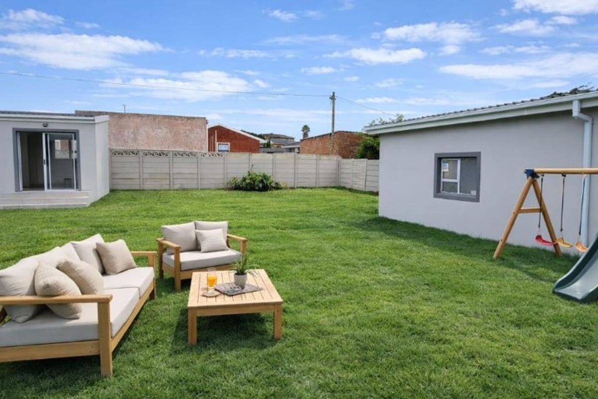 A spacious rear garden featuring a well-maintained lawn, enclosed by precast concrete boundary walls, with access to the main dwelling and outbuilding.