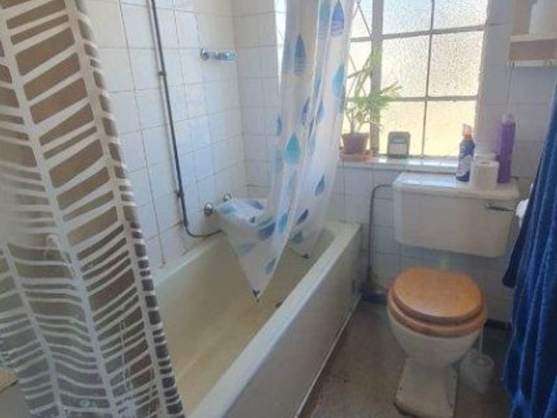 A functional bathroom featuring a bathtub with an overhead shower, a standard toilet, and tiled wall finishes, requiring cosmetic updates.