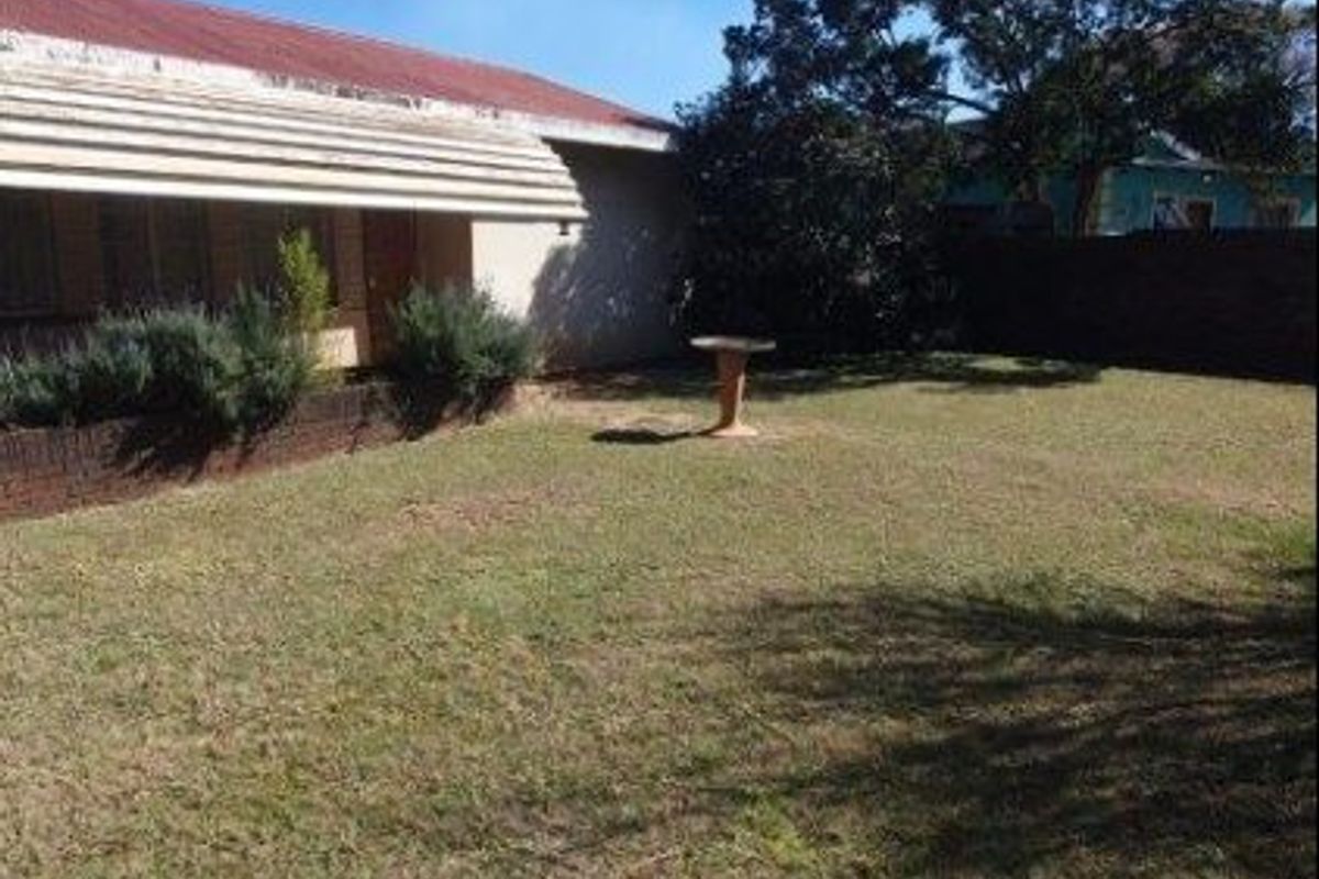 A rear garden area featuring a lawn, a brick boundary wall, and a metal window awning attached to the house exterior.
